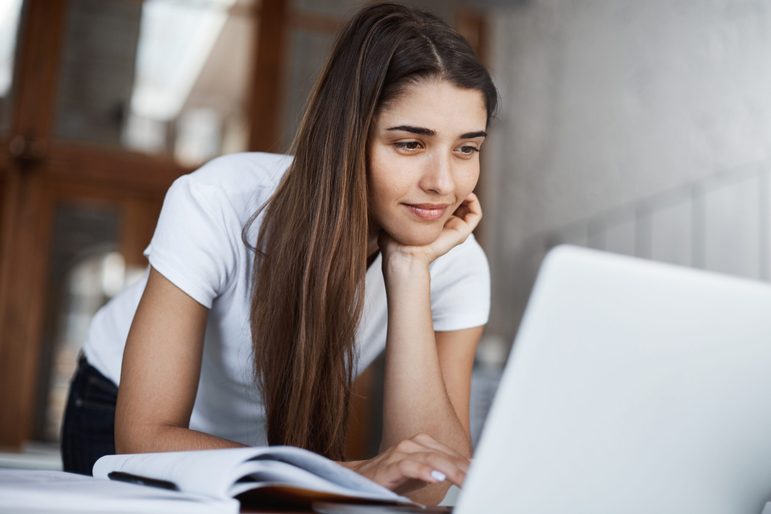 Happy young woman using laptop to scroll through tons of social media posts and photos smiling.